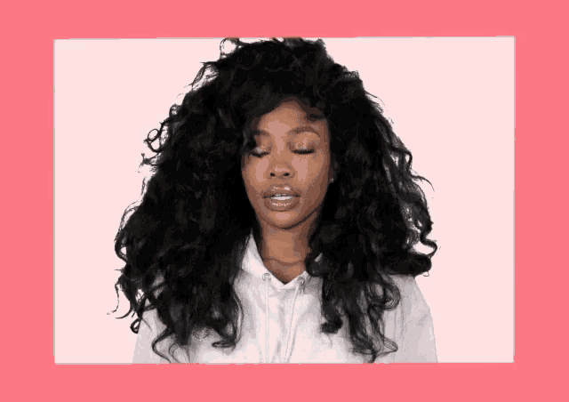 a woman with curly hair is wearing a white hoodie and has her eyes closed