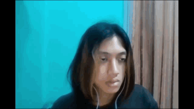 a woman is wearing headphones and making a funny face while sitting in front of a blue wall .