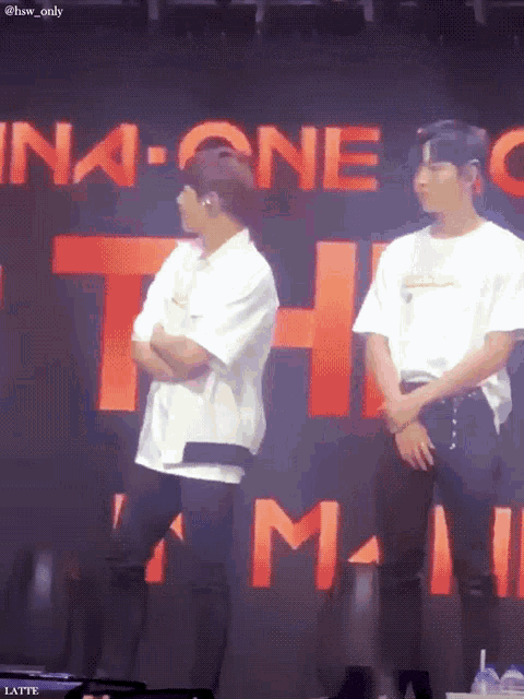 two men are standing in front of a large red sign that says ina one