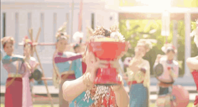 a woman in a colorful dress is holding a red bowl over her head