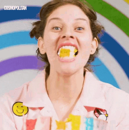 a woman wearing a pink shirt with a smiley face on it is eating a gummy bear .