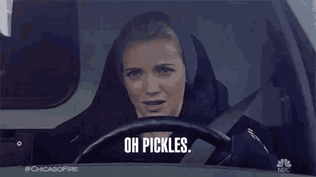 a woman is sitting in the driver 's seat of a car and saying oh pickles .