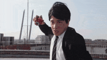 a man in a suit and tie is standing on a rooftop holding a red object in his hand .