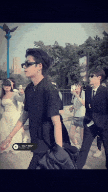 a man wearing sunglasses and a black shirt has a sticker on his shirt that says ' tb3 '