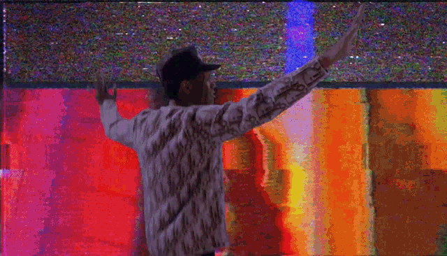 a man in a baseball cap is dancing in front of a colorful screen .