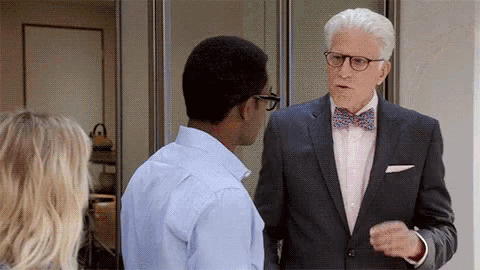 a man in a suit and bow tie is talking to another man while a woman looks on .