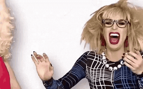 a drag queen wearing glasses and a plaid shirt is making a funny face with her mouth open .