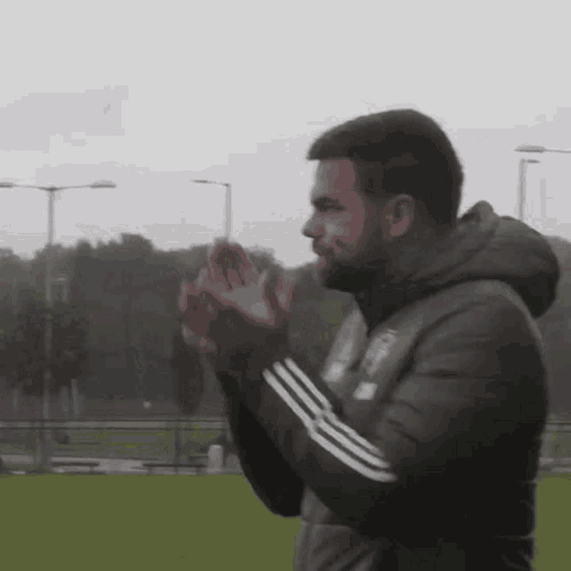 a man with a beard is clapping his hands on a field .
