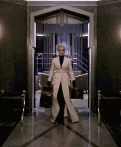 a woman in a white coat is walking through a doorway holding a suitcase