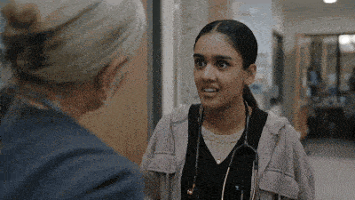 a nurse with a stethoscope around her neck is talking to another nurse in a hospital hallway .