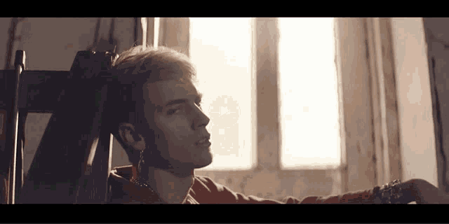 a man is sitting in a chair in front of a window with a play button on the screen