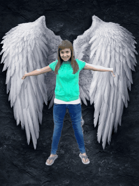 a girl wearing a green shirt and blue jeans has white angel wings on her arms