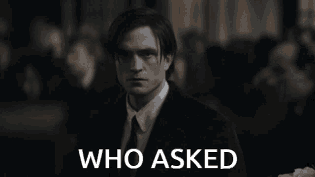 a man in a suit stands in front of a sign that says " who asked "