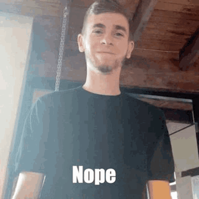a young man in a black shirt is standing in front of a wooden ceiling and making a funny face .
