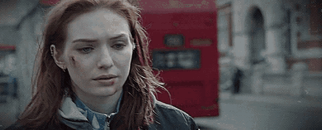 a woman with a bruise on her face is standing on a street next to a red bus .