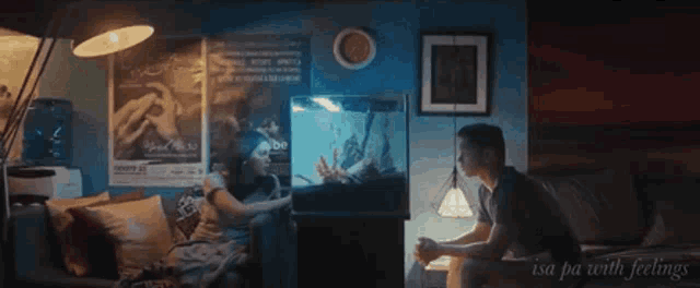 a man sits on a couch in front of an aquarium with the words isa pa with feelings on the bottom