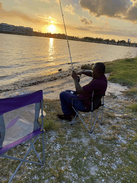 a man sits in a folding chair holding a fishing rod