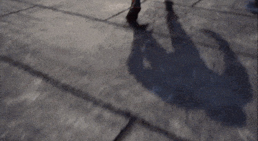 a person 's shadow is cast on the sidewalk while they walk .