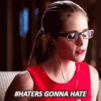 a woman wearing glasses and a red tank top is sitting on a couch and saying `` haters gonna hate '' .