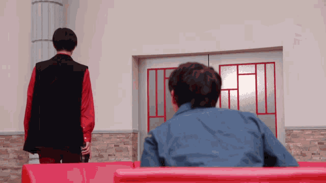 two men are standing next to each other in front of a red door