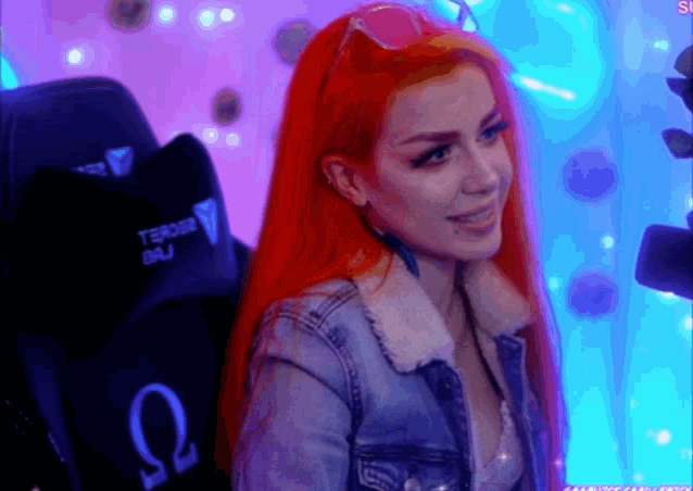 a woman with red hair is sitting in front of a gaming chair with the letter omega on it