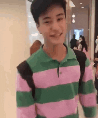 a young man wearing a pink and green striped shirt is smiling and looking at the camera .