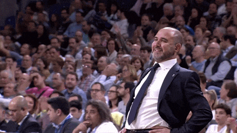a man in a suit and tie stands in front of a crowd at a basketball game