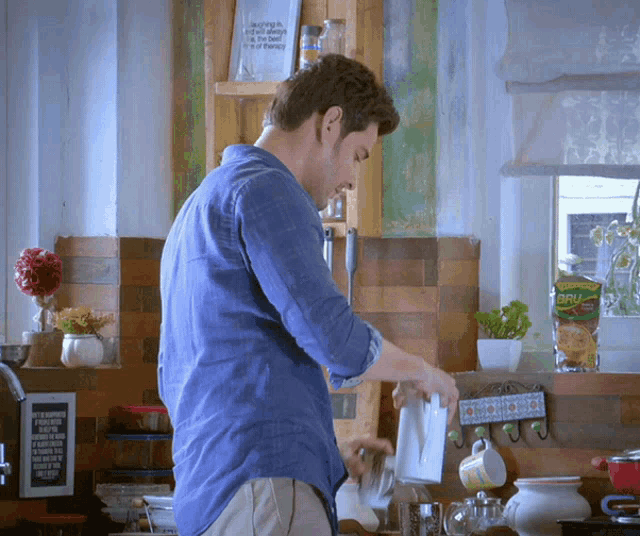 a man in a blue shirt is pouring something into a mug in a kitchen