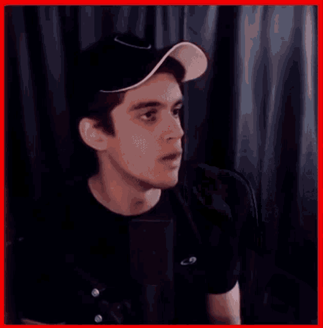 a young man wearing a hat and a black shirt is making a funny face .