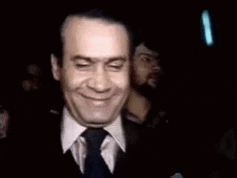 a man in a suit and tie is smiling in a dark room with other men .