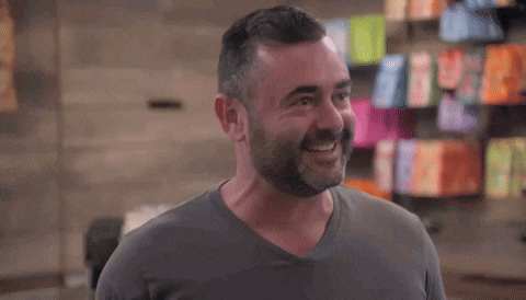 a man with a beard is smiling and looking at the camera while wearing a grey shirt .