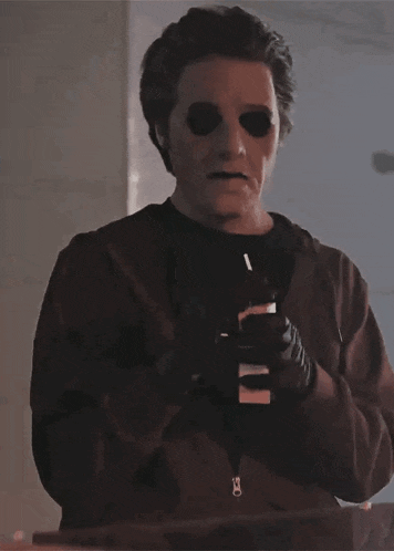 a man with black eyes is holding a cell phone and a cigarette