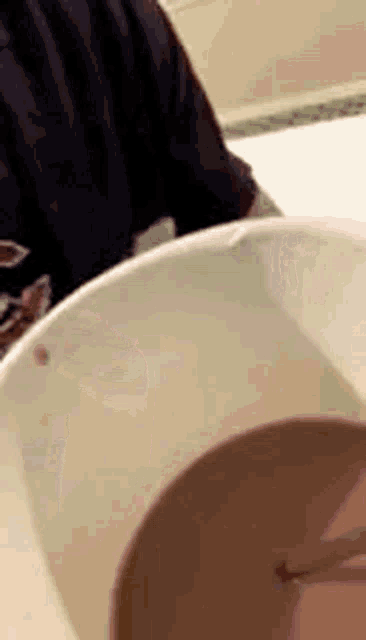 a person is sitting at a table with a cup of chocolate milk and a spoon in it .