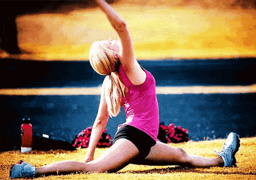 a woman in a pink tank top is doing a split on the grass