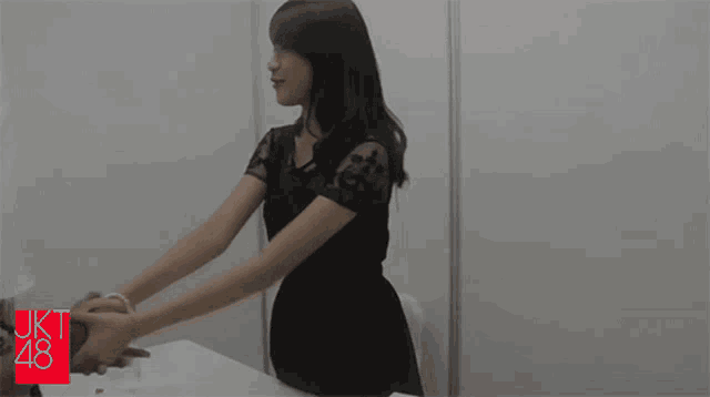a woman in a black dress shakes a man 's hand in front of a wall that says jkt 48