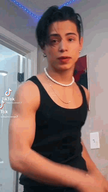 a young man wearing a pearl necklace and a black tank top .