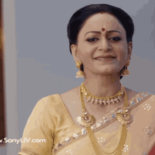 a woman with a red dot on her forehead is wearing a yellow top and gold jewelry