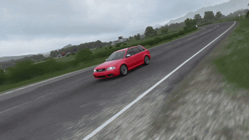 a red car is driving down a road with trees in the background