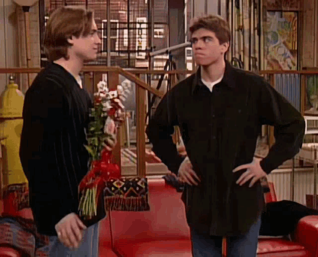 two men are standing next to each other in a living room with one holding a bouquet of flowers