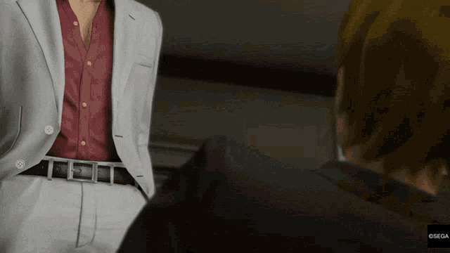 a man in a suit and red shirt is talking to another man in a black shirt