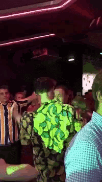 a group of people are dancing in a dark room and one of them is wearing a yellow shirt with bananas on it