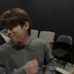 a man in a grey sweater is sitting in a chair and covering his face with his hand .