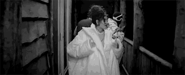 a woman in a white coat and pearls is walking down a hallway .