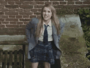 a girl in a school uniform is giving the middle finger in front of a brick wall