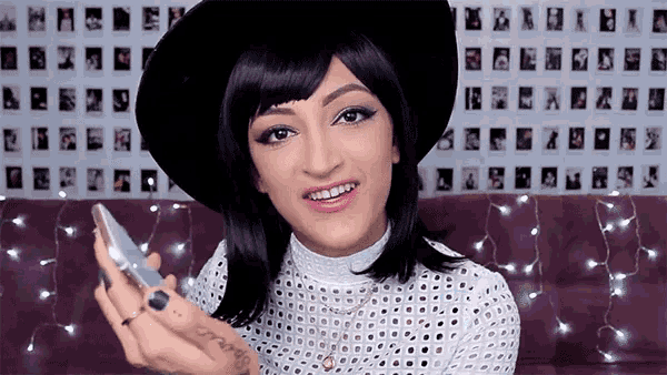 a woman wearing a black hat and a white top has a tattoo on her arm that says " because "