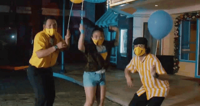 a group of people wearing face masks and holding balloons are dancing on a street .