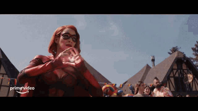 a woman in a red superhero costume is standing in front of a crowd and a sign that says prime video on the bottom