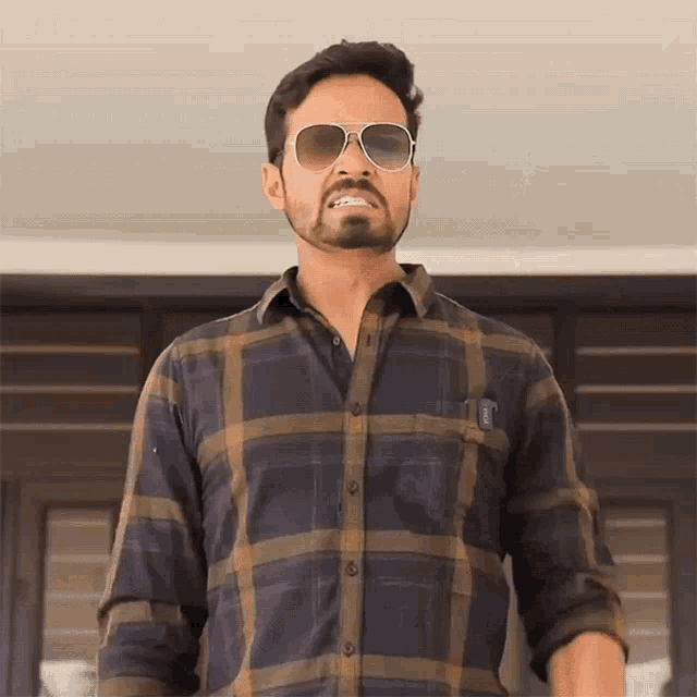 a man wearing sunglasses and a plaid shirt has a pocket with a sticker that says ' a ' on it