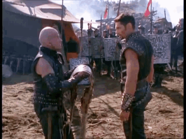 two men are standing next to each other in a field talking to each other .