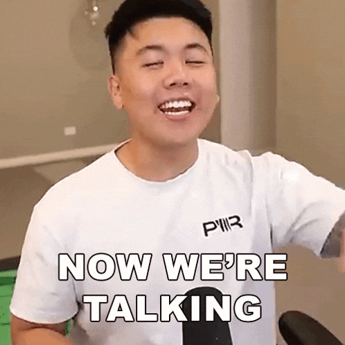 a man wearing a white t-shirt is smiling and says `` now we 're talking '' .